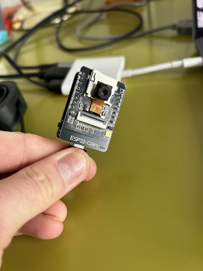 An esp32 module held in a hand on a green background 