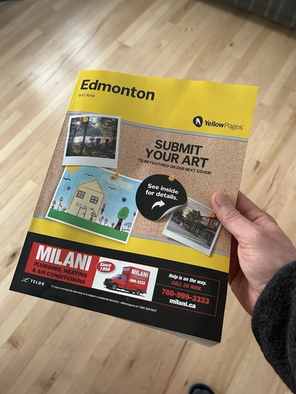 An Edmonton phone book held in a hand over a maple wood floor.
