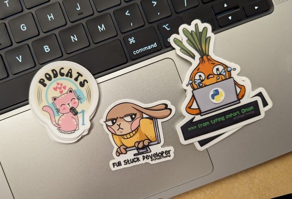 Stickers on top of laptop keyboard.
Podcast: a cat with headphone and mic
Full Stuck Developer: a Bunny looking disgruntled, stuck on a computer screen
>>> from typing import Onion
An Onion crying behind a laptop with Python logo