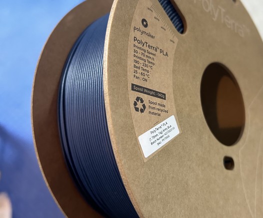 A roll of dark blue 3d printing plastic filament on a cardboard spool. The background is lighter blue
