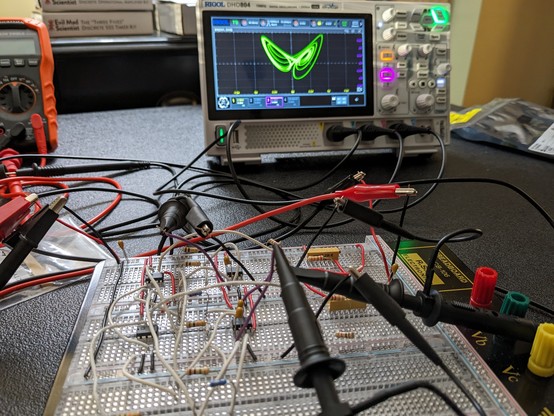 An electronic circuit with probes connected. An oscilloscope displays the Lorenz attractor butterfly shape.