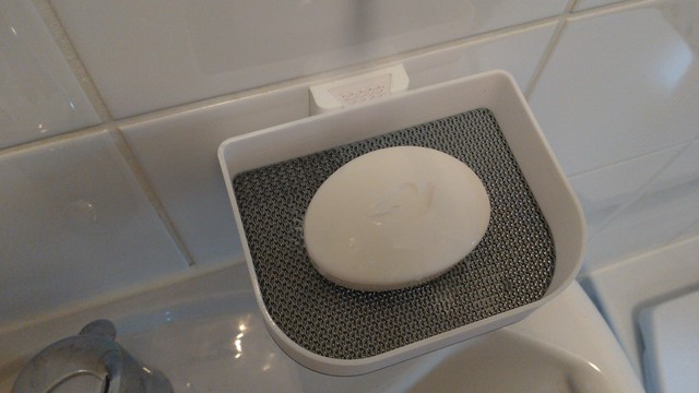3d printed white soap dish with perforated bottom, attached to a tiled white wall with a dovetail shape, a white soap bar (with a dove embossed on it by incident) lies in the dish.