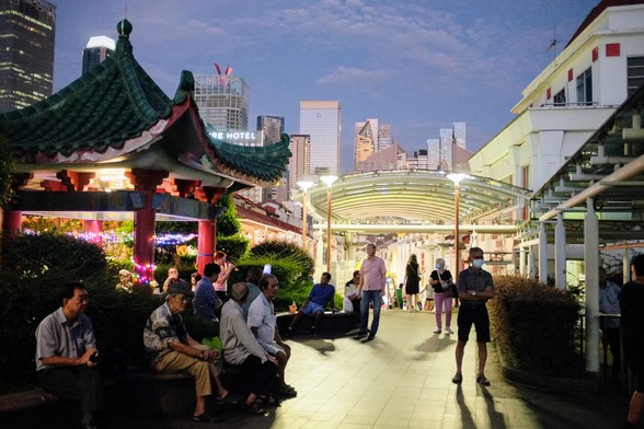 Buskers performing at a Chinese pavilion with public around, under twilight sky and distant high rise cityscape. 