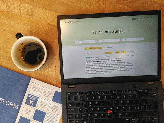A coffee cup. A laptop with a website open with the title "Vernehmlassungen". A booklet on the Sustainable Development Goal with the page open on SDG 16 Peace Justice Strong Institutions 