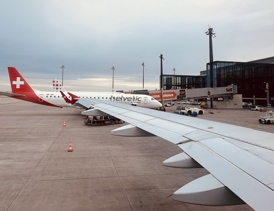 The branding for Helvetic Airways does not leverage Helvetica font - photo of an aircraft from Helvetic Airways on the runway at Berlin BER Airport ready for an early morning flight. The plane depicts the Swiss flag prominently on the tail wing.