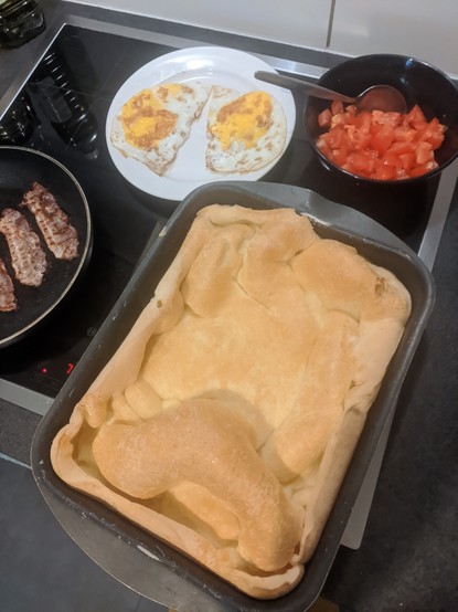A baking tin of montanha russa with fried eggs, baconeand tomatoes on the side