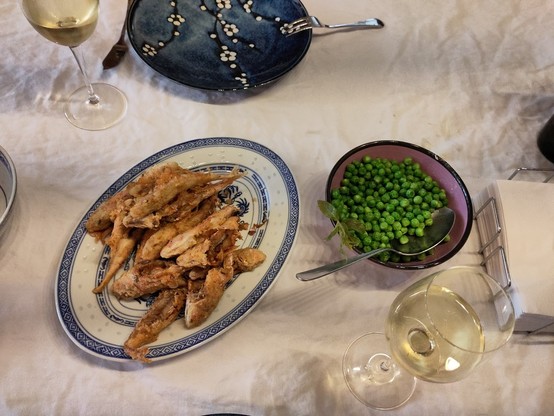 A plate of deep-fried small fishies, a bowl of fresh peas. In the background, a glass of white wine and a plate.