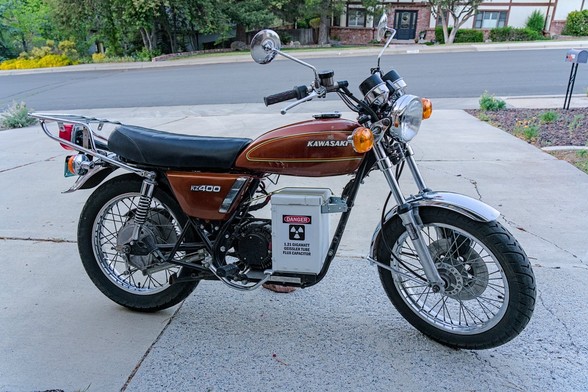 Color photo of a classic Japanese commuting motorcycle for the 1970s. It's a copper brown color. On the gas tank it says, 