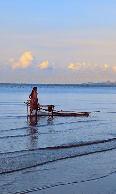 Photo of a young woman catching fish fingerlings using an improvised bamboo contraption with fish net while walking through the coastline.