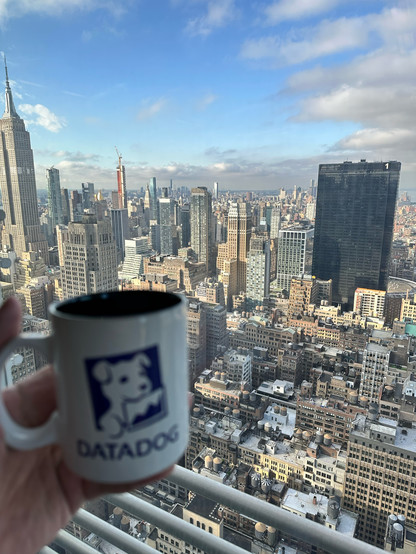 A man holding a Datadog mug in front of the New York skyline. 
