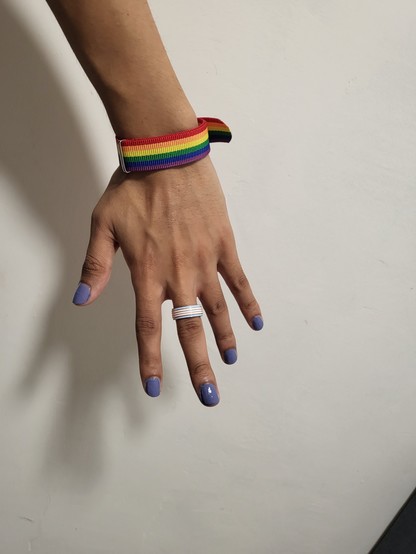 photo of my hand with a trans flag ring on, blue nail polish and a rainbow bracelet!!! (don't ask how many times it took me to get a photo that I liked, hand dysphoria hitting real hard frfr)