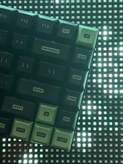 A close-up of a computer keyboard with black and green keycaps against an illuminated green LED grid background.
