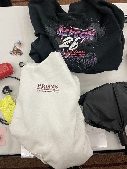 A Defcon 26 sweatshirt, a PRISMS Princeton International School of Mathmatics and Science sweatshirt, a black umbrella