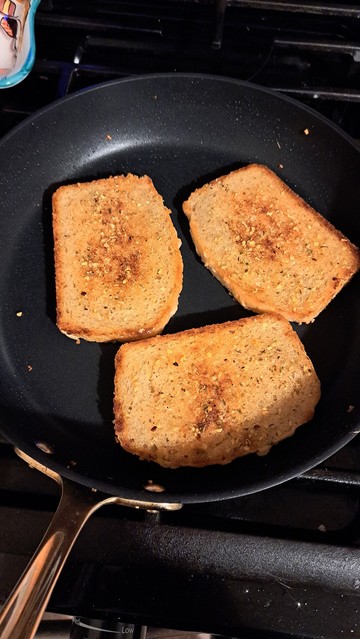 The slices of bread, browned in the top with seasoning in a large gray pan. 