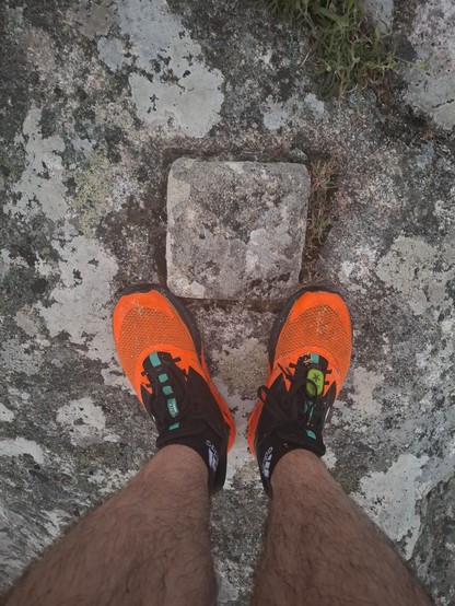 Runner legs with orange shoes, near the stone which marks the pick of the mountain