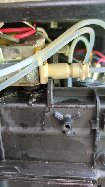 Picture of the inside of a coffee machine with hoses and wires running around. A white plastic clamp is in the foreground with a bunch of evidence of leaking on one side (corroded metal, water).