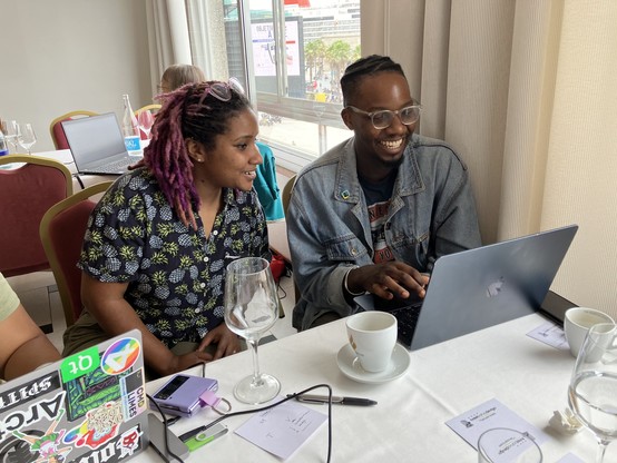 Dawn and Kudzayi at a table side by side, looking at a laptop, smiling