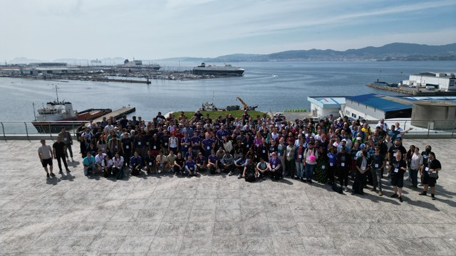 A group of people standing on a terrace with a beautiful landscape view of the mountains, boats and ships in the background.