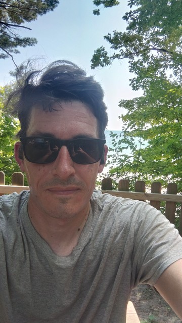 A selfie. I'm wearing a grey shirt and sunglasses. You can see Lake Michigan in the distance. 