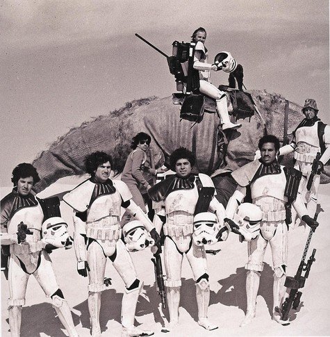 Stormtrooper actors in Tunisia desert in 1977 with their helmets off, hair flowing in the wind, and one is smoking. 