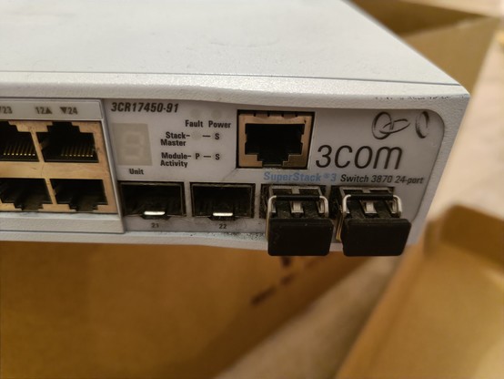 Picture of part of a big network switch. It is of the brand 3COM (I think) and has a few ethernet and other unknown ports.