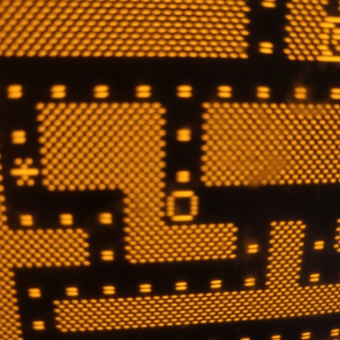 A close-up of an amber monitor displaying a Pac-Man clone for the ZX81