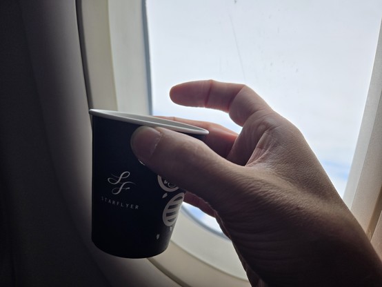 Holding up a Starflyer-brandef cup of coffee in front of a plane window mid-flight.