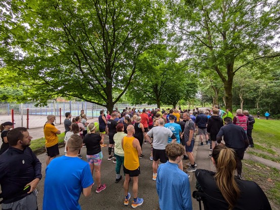 The view from the back. Many runners line up on a tree-lined asphalt path listening to the Run Director give the introduction speech.