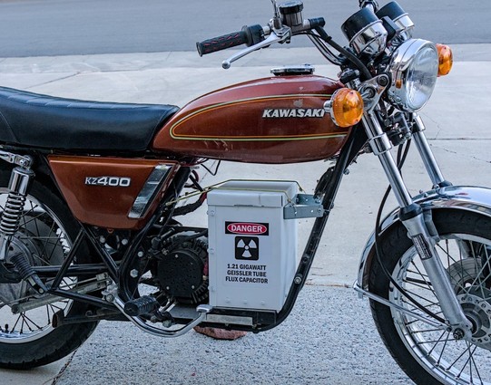 Color photo of a classic Japanese commuting motorcycle for the 1970s. It's a copper brown color. On the gas tank it says, 