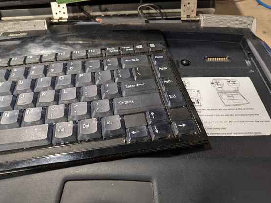 An old Toshiba laptop with the lid broken off. The wireless keyboard is at an angle set on the left side of the laptop. You can clearly see the instructions on how to use the keyboard and the contacts for charging and data when the keyboard is connected. I'm not transcribing the instructions because they really don't matter here.
