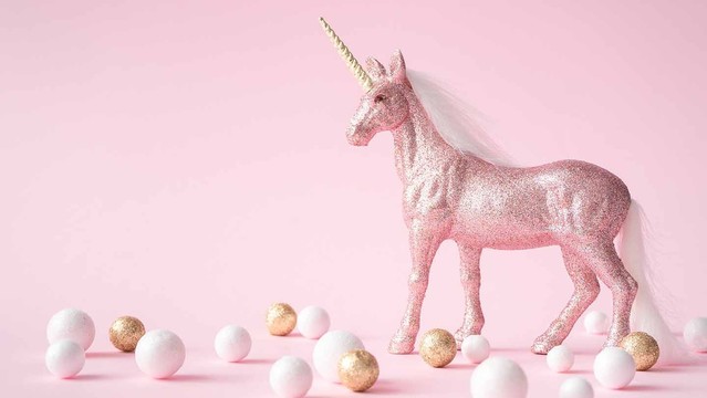 A sparkly pink unicorn with a gold horn and white mane and tail surveys white and gold spheres on a pink background