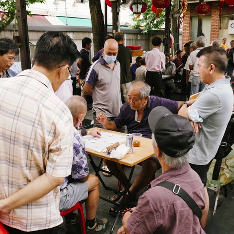 Two elderly men playing a checkers game surrounded by several onlookers. 