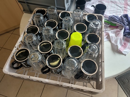 Ein Spülmaschinenträger, im Schachbrettmuster bestückt mit abwechselnd schwarzen Tassen und Ikea Gläsern. Das gleichmäßige Muster wird durch einen neon gelben CYBER Becher anstatt eines Glases unterbrochen.
