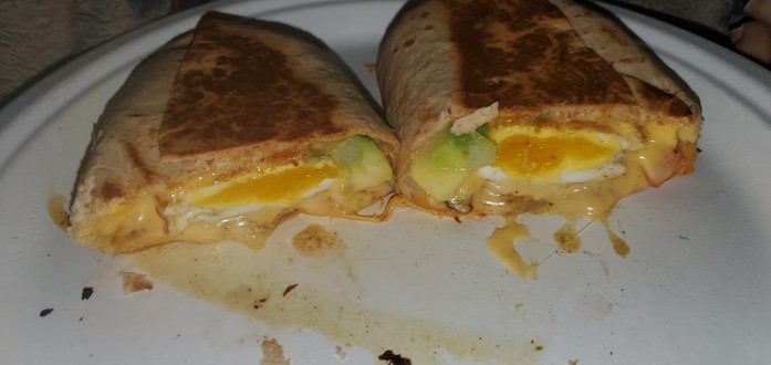 Breakfast burrito with semi-poached medium fried egg, avocado, tomato, onion, American cheese, and 3-pepper Colby Jack cheese. It's cut in half to show the cross-section of fillings.