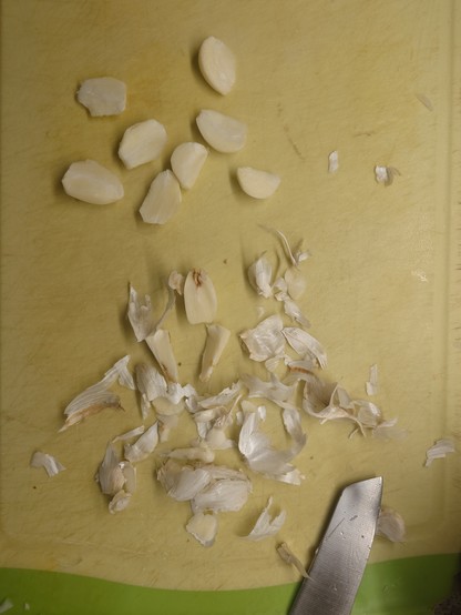 Chopping board with garlic cloves and some bad ones at the side amongst the peelings.