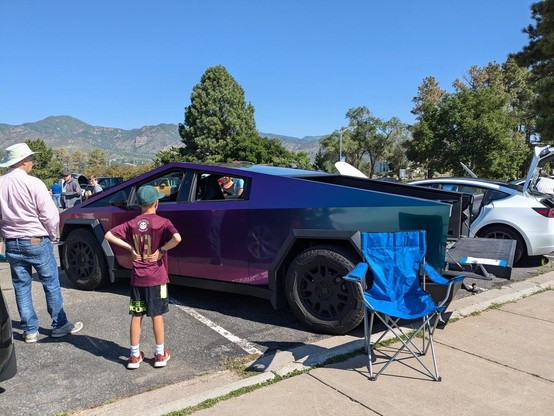 Tesla cybertruck with a purple pearl wrap, being displayed at a car show. A couple of people are standing looking at it with their backs to the camera.