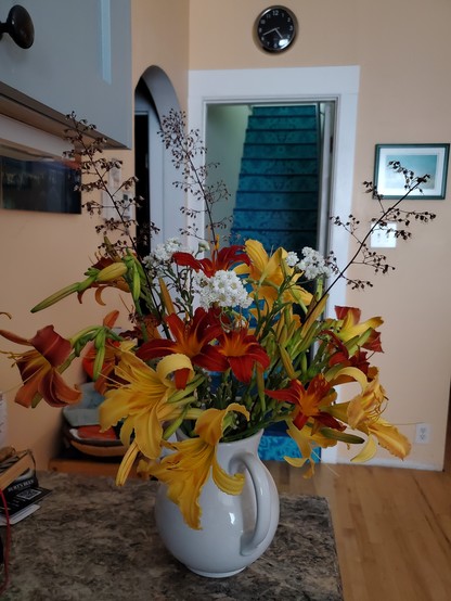 White pitcher with red and orange daylilies along with 3 taller stems of huechera and a 3 small, white flowers 
