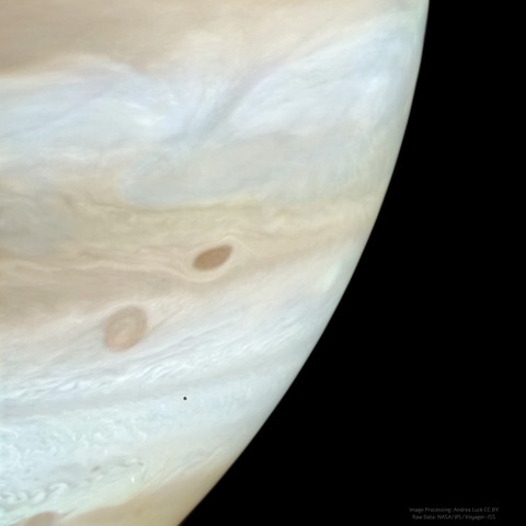 A composite image showing the small, potato-shaped satellite of Jupiter, Amalthea, transiting over the gas giant. Jupiter appears orangish with white bands of clouds and a swirling atmosphere. Amalthea appears grey, as only one filter was used. As seen by NASA Voyager 2 in 1979!