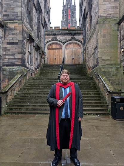 Graduate standing in historic academic courtyard in graduation gown (New College, Edinburgh)