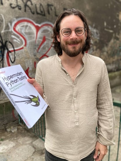 Me holding a physical copy of my O'Reilly book Hypermodern Python Tooling in my hands, photographed in the streets of Poznan