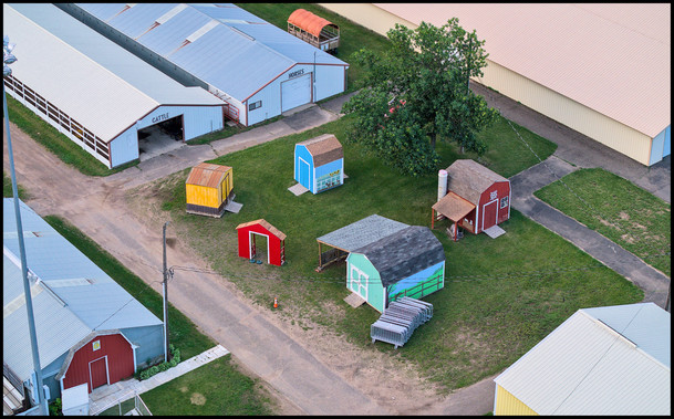 Aerial view of play area at rural race track, including a number of child sized barns and playhouses painted in bright colors.