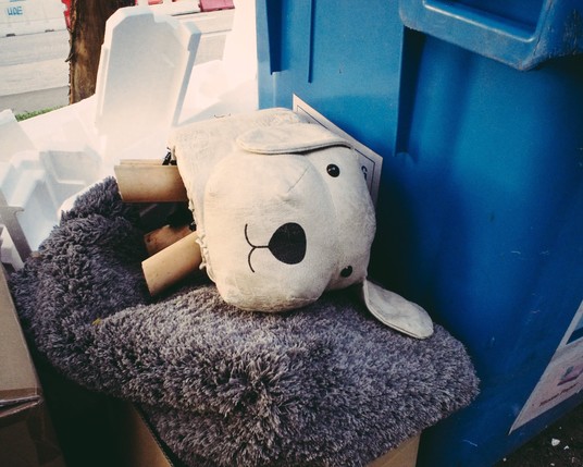 A decorative stuffed animal abandoned at next to the recycling bin 