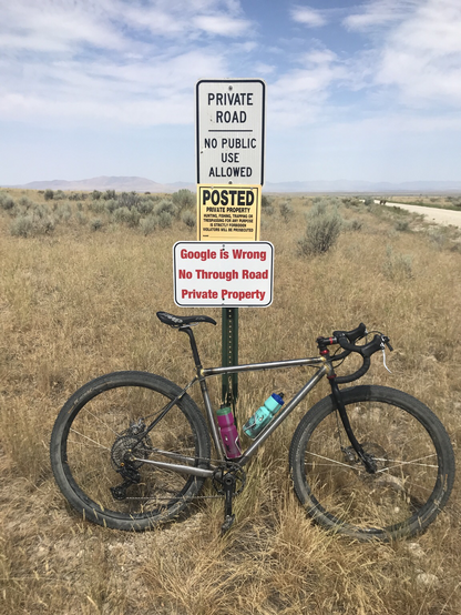 A bicycle leans against a sign post with multiple signs that indicate the road beyond is private. One says specifically “Google is wrong. No through road. “