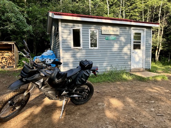 a dirty Zero FX parked in front of a cabin in the woods.