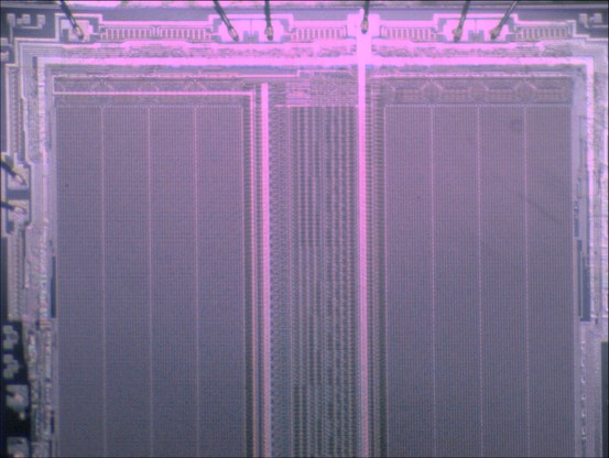 A view threw the microscope on a price of silicon. On the outside are some unregular structures and bonding wires. The middle shows some large regular pattern. The manufacturing structure is so big, that you can almost see the individual EPROM cell.