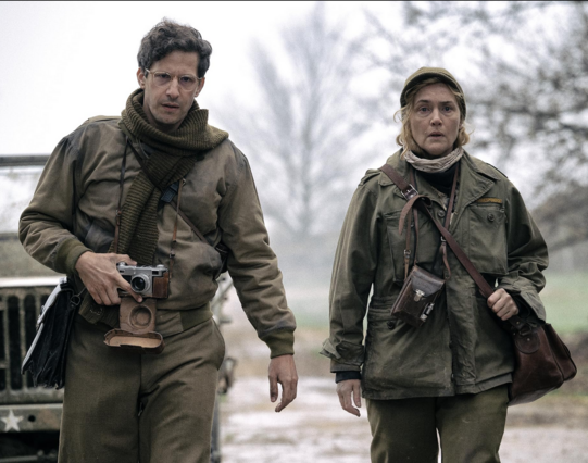 A frame from the movie Lee featuring Andy Samberg and Kate Winslet in world war 2 military fatigues and carrying classic cameras, a Leica and a Rolleiflex respectively.