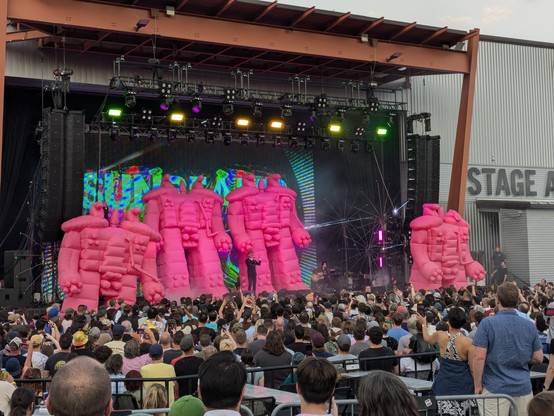 Wayne Coyne of the Flaming Lips standing on stage surrounded by large pink inflatable robots
