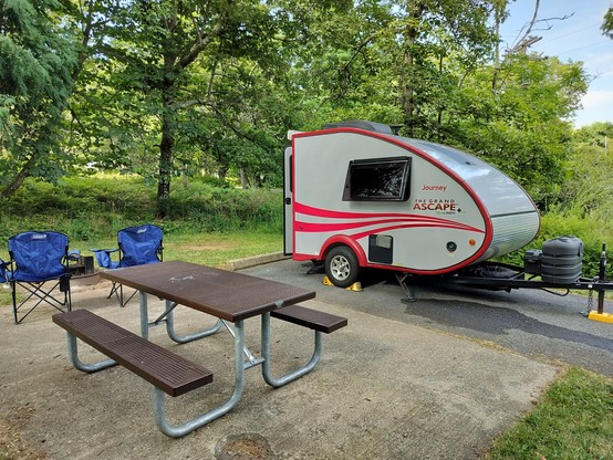 small red camper parked at campsite with camp chairs and a picnic table