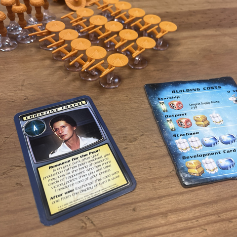 Getting ready to play: the player has lined up their orange starship pieces in the top of the picture. A ‘Christine Chapel’ character card and a ‘Building Costs’ sit below them. 