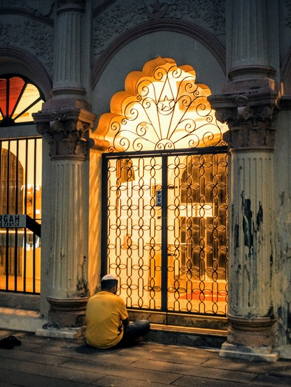 Man seated praying outside the closed gates of a mosque 